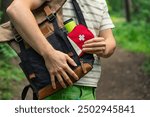 Close-up of a person taking a first aid kit out of a backpack while on a forest trail, highlighting outdoor preparedness and safety. 