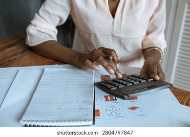 A close-up of a person using calculator with documents and a notepad on wooden desk, depicting business or finance setting.