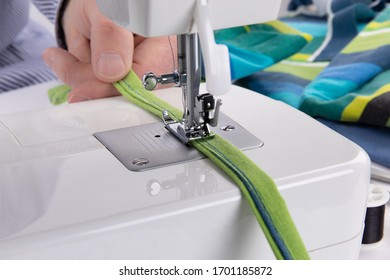 closeup of a person using a sewing machine to sew the tie strings of a home made covid-19 mask