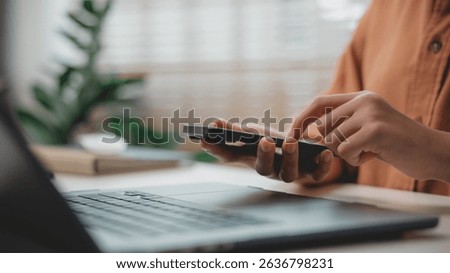 Close-up of person using smartphone while working on laptop, representing digital communication, mobile productivity, smart office, multitasking, and remote work lifestyle.