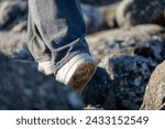 Close-up of a person walking on rocky pier, only foot in white outdoor shoe visible. Sense of mystery and adventure. Contrast of white shoe against rugged path symbolizes journey and  challenges. 