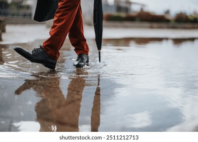 Close-up of person walking through puddle with an umbrella on a rainy day, their reflection visible in the water. - Powered by Shutterstock