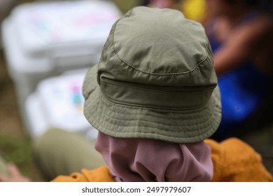 Close-up of a person wearing a green hat and a scarf, focusing on the back of their head at an outdoor gathering. - Powered by Shutterstock