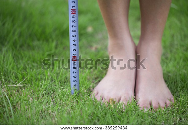 Close-up of person\'s feet measuring height with\
measurement tape.