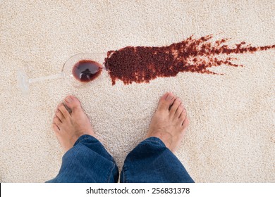 Close-up Of A Person's Feet Standing Near Red Wine Spilled On Carpet