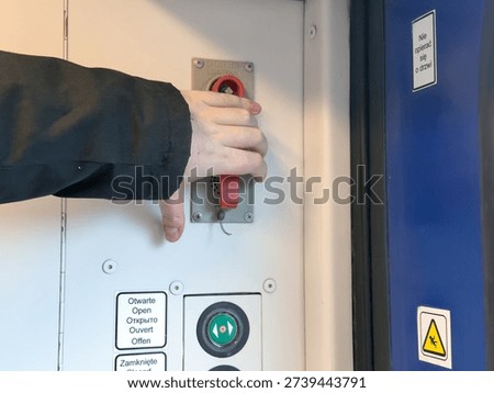 Close-up of a person's hand activating the red emergency lever on a train's door control panel, signifying passenger safety and operational procedures