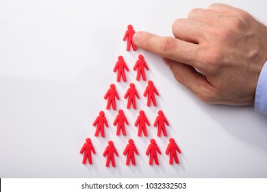 Close-up Of A Person's Hand Arranging Red Human Figures In Triangular Shape On White Background