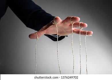Close-up Of Person's Hand Controlling Puppet Against Gray Background