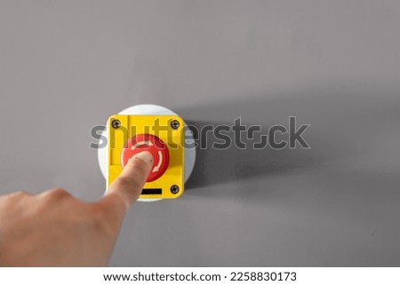 Close-up Of Person's Hand Emergency Bell On Table. An industrial emergency stop button with a finger pressing down