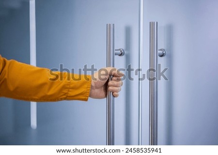 Close-up of a person's hand gripping a metallic handle to open a glass door, emphasizing themes of access, entry, or beginning a new opportunity.