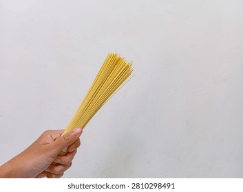 a close-up of a person's hand holding a bundle of raw, uncooked spaghetti. on a white background.