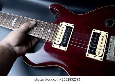 Close-up of a person's hand holding an electric guitar with a dark red, glossy body. Musical instrument with metallic hardware in a studio or stage setting. - Powered by Shutterstock