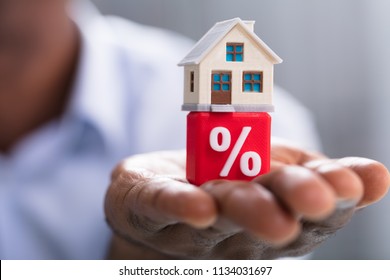 Close-up Of A Person's Hand Holding Miniature House On Red Percentage Block