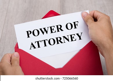 Close-up Of A Person's Hand Holding Power Of Attorney Document In Red Envelope