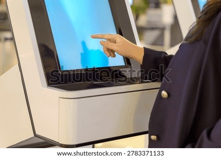 Close-up of a person's hand interacting with a digital touch screen on a modern white self-service kiosk, likely for check-in or service in a public place