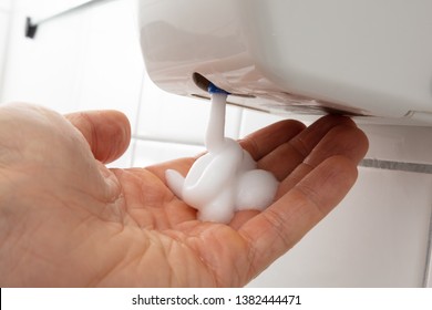 Close-up Of Person's Hand With Liquid Soap Dispenser On Tiled Wall