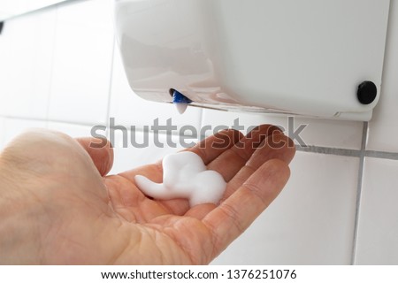 Close-up Of Person's Hand With Liquid Soap Dispenser On Tiled Wall