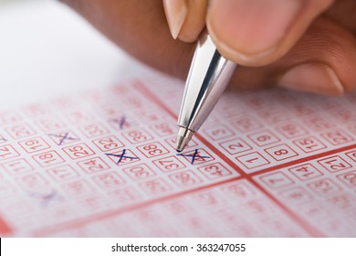 Close-up Of Person's Hand Marking Number On Lottery Ticket With Pen