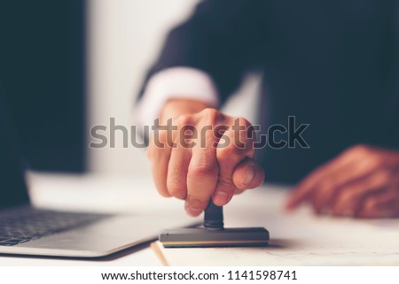 Close-up Of A Person's Hand Stamping With Approved Stamp On Document At Desk, notary or business people work from home, isolated for coronavirus COVID-19 protection