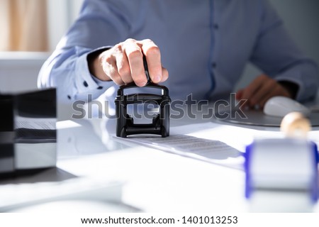 Close-up Of A Person's Hand Stamping With Approved Stamp On Document At Desk