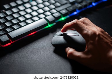 Close-up of a person's hand using a computer mouse next to a keyboard with colorful back lighting.