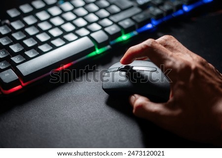 Close-up of a person's hand using a computer mouse next to a keyboard with colorful back lighting.