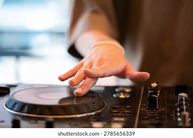 Close-up of a person's hand using a DJ mixer and turntable jog wheel, mixing music at an event.