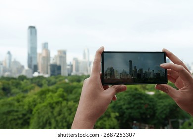 Close-up of a person's hand using a mobile phone to take a picture of a city view with tall buildings.