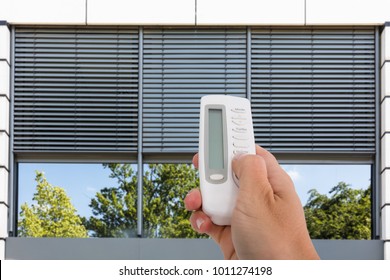 Close-up Of A Person's Hand Using Remote To Open Window Shutter
