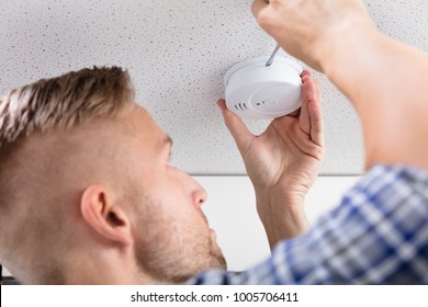 Close-up Of A Person's Hand Using Screwdriver To Install Smoke Detector On Ceiling At Home