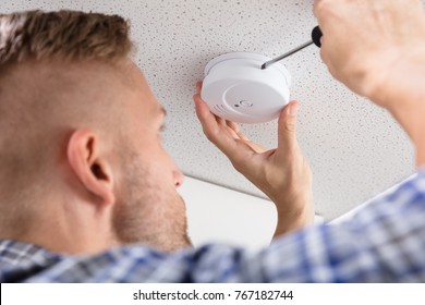 Close-up Of A Person's Hand Using Screwdriver To Install Smoke Detector On Ceiling At Home