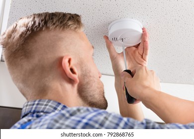 Close-up Of A Person's Hand Using Screwdriver To Install Smoke Detector On Ceiling At Home