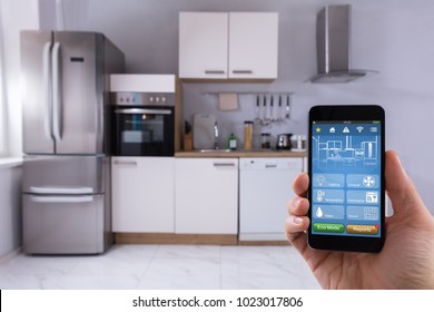 Close-up Of A Person's Hand Using Smart Home System On Mobilephone In Kitchen