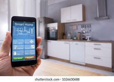 Close-up Of A Person's Hand Using Smart Home System On Mobilephone In Kitchen