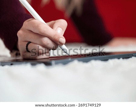 Close-up of a person's hand using a white stylus on a digital drawing tablet at a creative workspace.