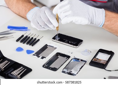 Close-up Of Person's Hand Wearing Glove Repairing Cellphone Using Screwdriver