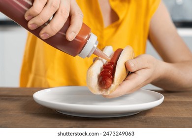 Close-up of a persons hands adding ketchup to a hot dog on a white plate, ready to eat, fast food lunch