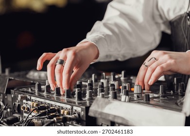 Close-up of a person's hands adjusting knobs and faders on a professional DJ audio mixer in a dim environment at a club or event.