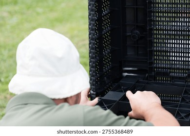 Close-up of a person's hands assembling black plastic outdoor furniture. They carefully connect pieces, showing detail and effort in the process.