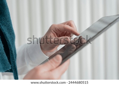 Close-up of a person's hands expertly navigating a tablet, with a glimpse of a teal scarf and white shirt indicating a smart, casual style.

