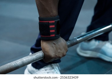 Close-up of a person's hands gripping a barbell, wearing a wrist support or strap. sneakers are visible, suggesting a workout session at a gym.                              - Powered by Shutterstock