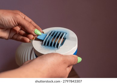 Close-up of a person's hands inserting a blue insecticide mat into an electric mosquito repellent vaporiser.