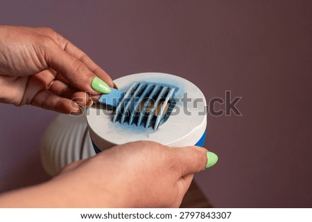 Close-up of a person's hands inserting a blue insecticide mat into an electric mosquito repellent vaporiser.