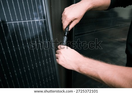 Close-up of a person's hands plugging together male and female MC4 connectors. The black cables are being connected to power a solar energy system installed on a residential fence