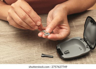 A close-up of a person's hands using a specialized cleaning brush to maintain a behind-the-ear hearing aid device for better performance and hygiene.