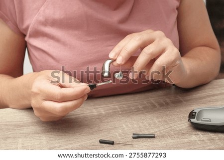 A close-up of a person's hands using a specialized cleaning brush to maintain a behind-the-ear hearing aid device for better performance and hygiene.