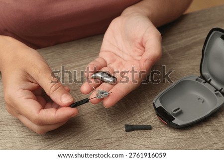 A close-up of a person's hands using a specialized cleaning brush to maintain a behind-the-ear hearing aid device for better performance and hygiene.