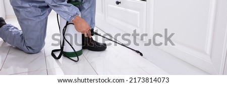 Close-up Of A Pest Control Worker's Hand Spraying Pesticide On White Cabinet