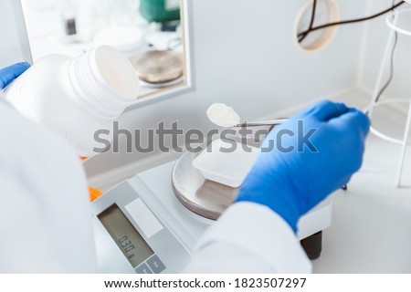 Closeup of pharmacist hand holding bottle while weighing white powder chemical in a laboratory