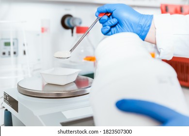 Closeup of pharmacist hand wearing blue gloves pouring white powder chemical on weighing scale in laboratory - Powered by Shutterstock